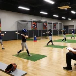Young athletes training at a hit club with pitching machines and coaches.